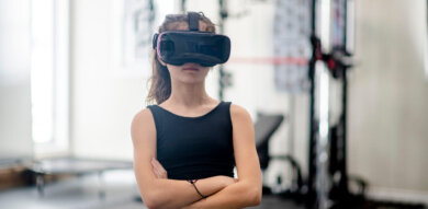 young white woman stands in gym with a VR headset arms crossed