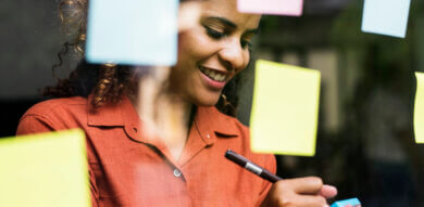 Woman of color User Researcher smiles while writing sticky note